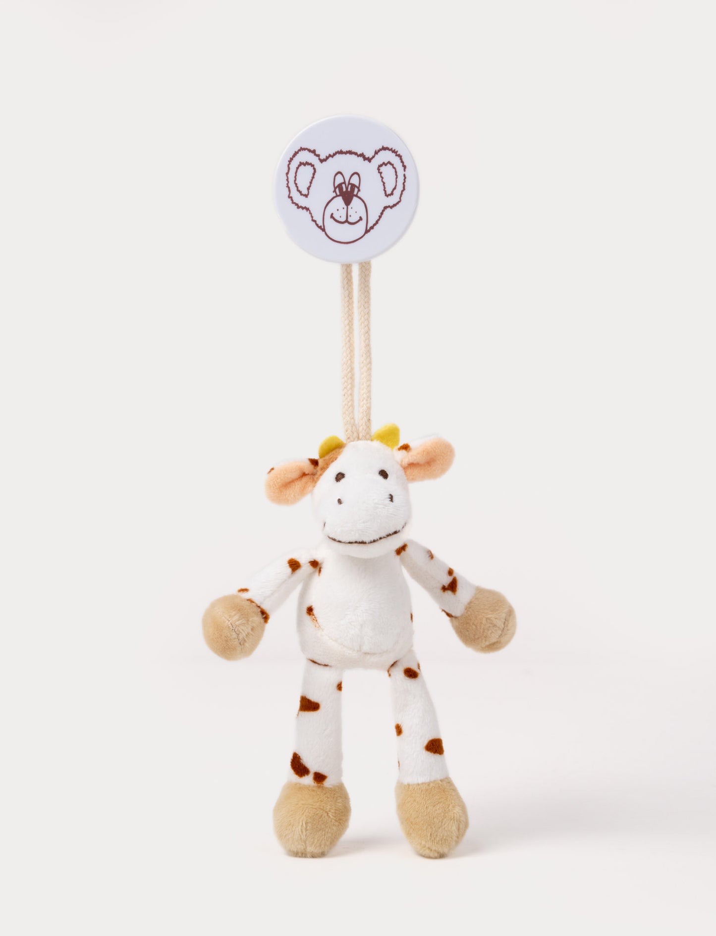 A plush cow clip toy with a white body, brown spots, beige hooves, and a round bear-illustrated clip.
