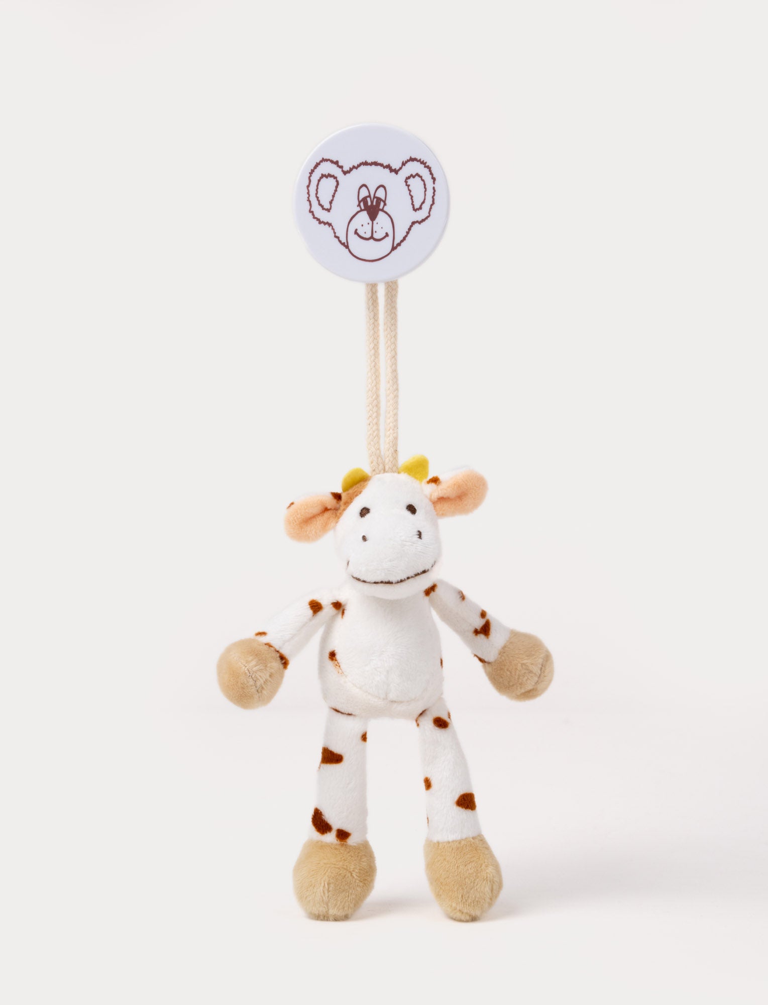 Image of A plush cow clip toy with a white body, brown spots, beige hooves, and a round bear-illustrated clip.