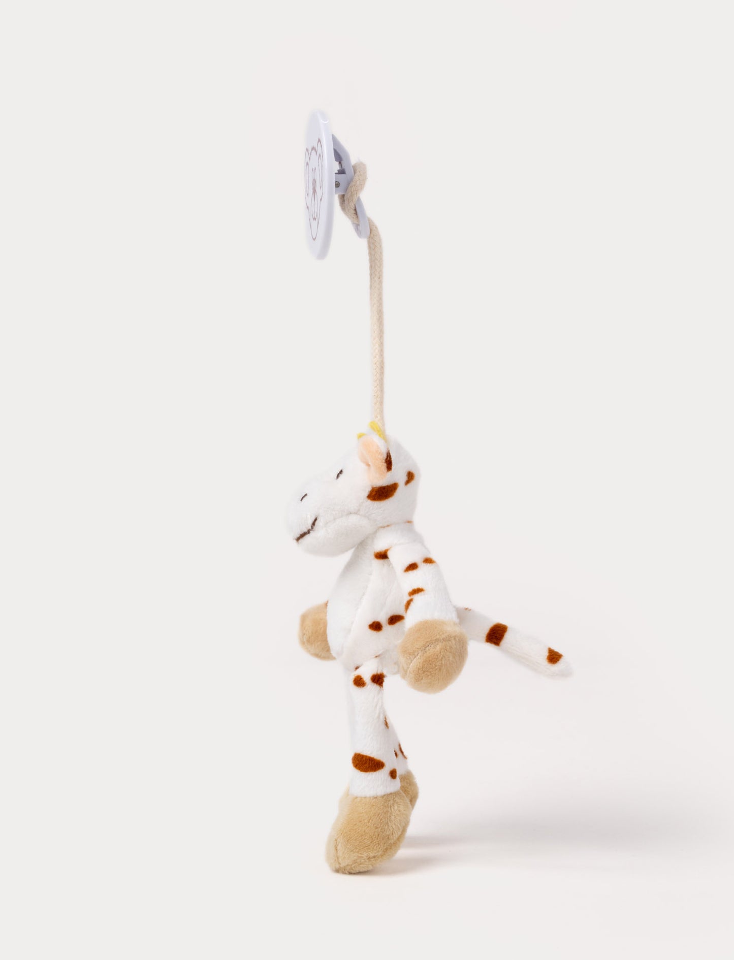 A plush cow clip toy with a white body, brown spots, beige hooves, and a round bear-illustrated clip.