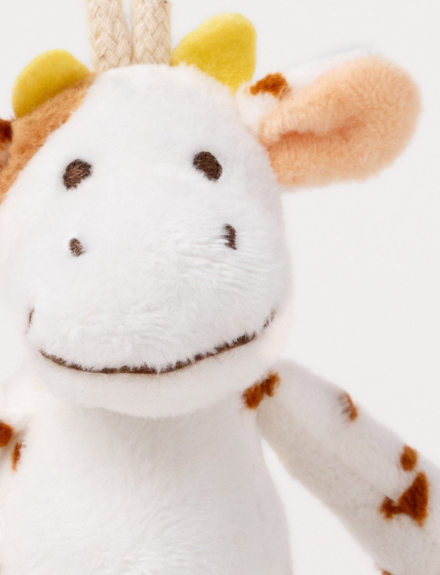 A plush cow clip toy with a white body, brown spots, beige hooves, and a round bear-illustrated clip.