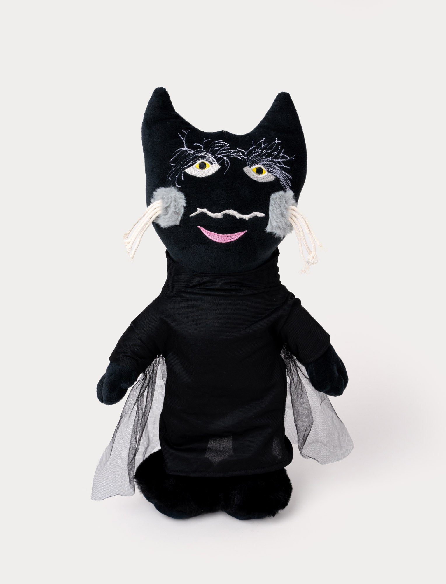 Image of A plush toy of a black cat wearing a dark outfit with mesh cape details and embroidered facial features.