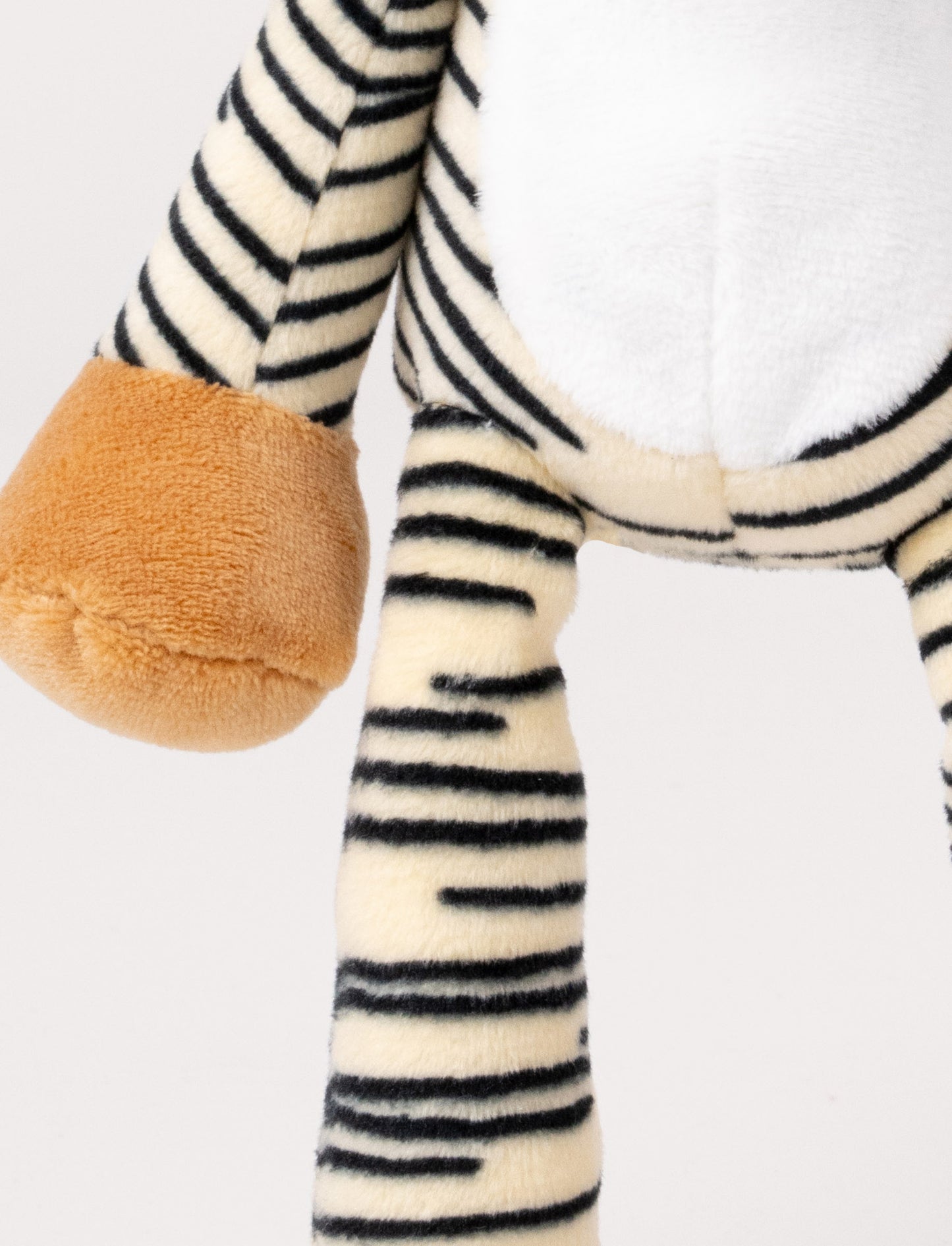 A plush tiger music box with black stripes, a white belly, beige paws, and a fabric loop for hanging