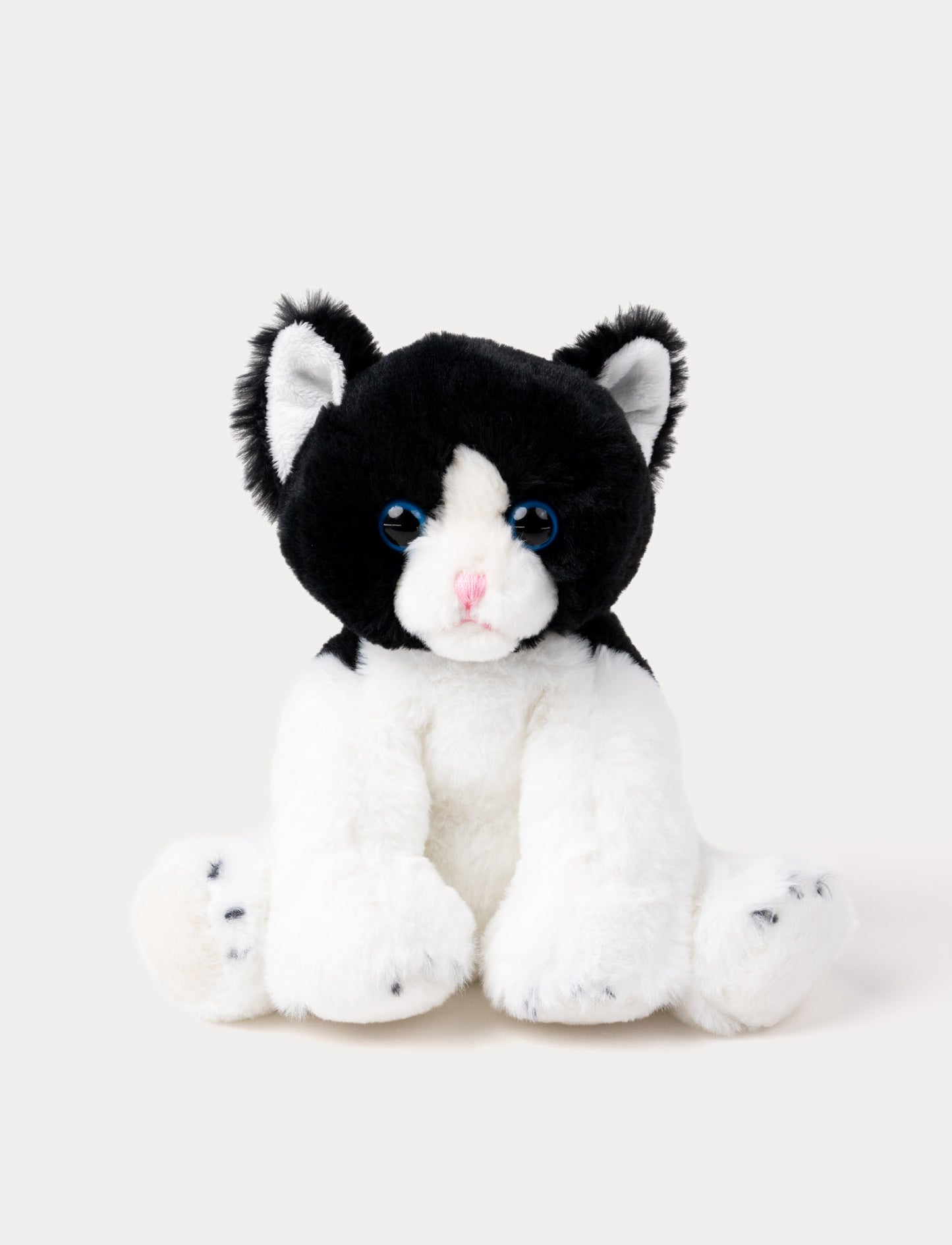 Soft black and white kitten plush with blue eyes, a pink nose, and white paws.