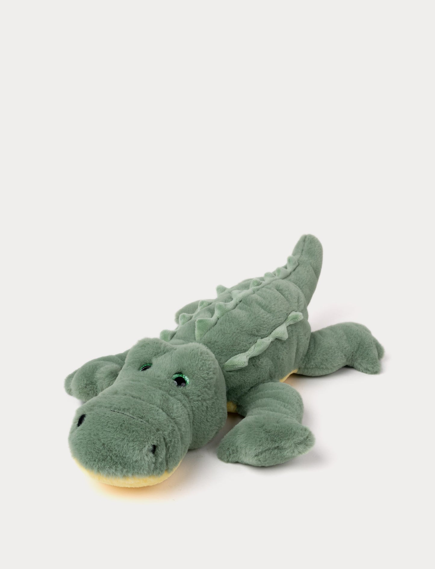 Soft plush alligator with green fur, embroidered eyes, and a textured back, lying down.