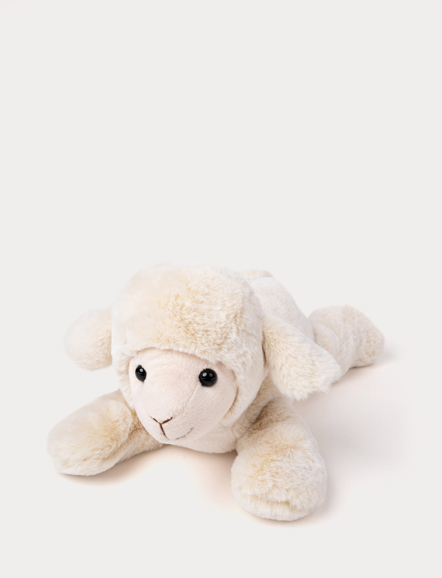 Soft plush lamb with cream-colored fur, black bead eyes, and a stitched smile, lying down.