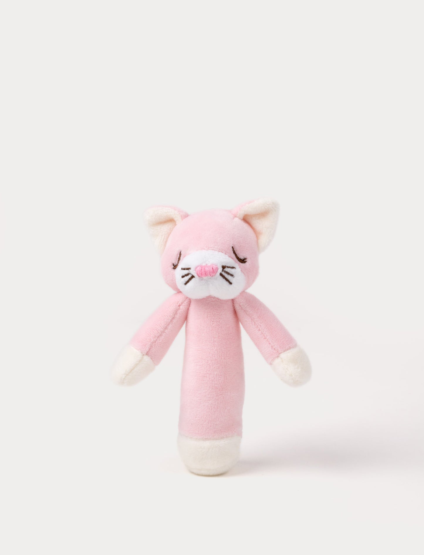 Soft plush cat rattle with a pink body, embroidered sleeping eyes, a white muzzle, and white accents on the hands and base.