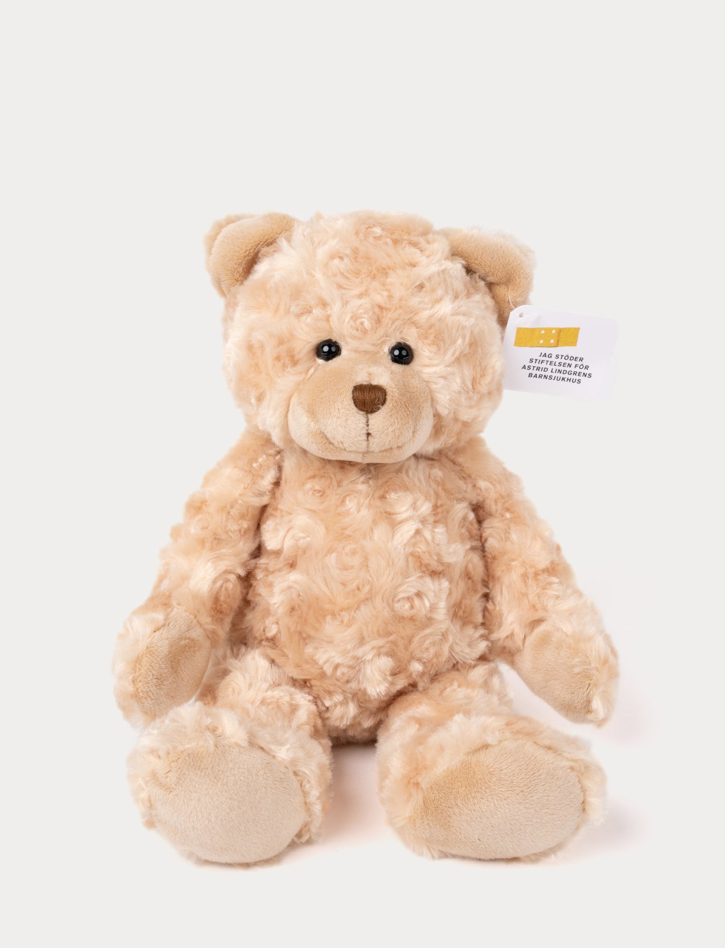 Soft, curly beige teddy bear with black eyes, a stitched brown nose, and a tag supporting a children's hospital.