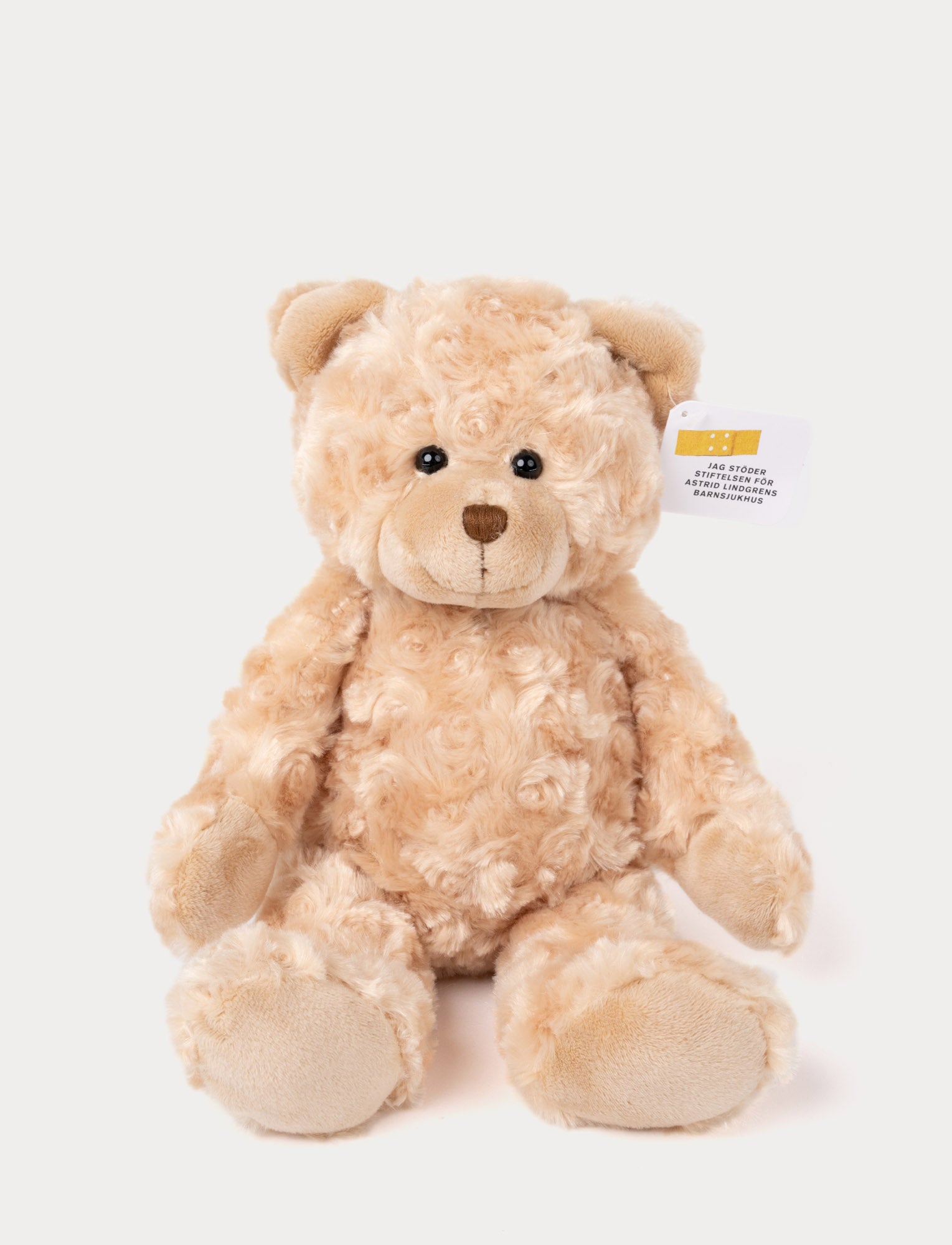  Image of Soft, curly beige teddy bear with black eyes, a stitched brown nose, and a tag supporting a children's hospital.