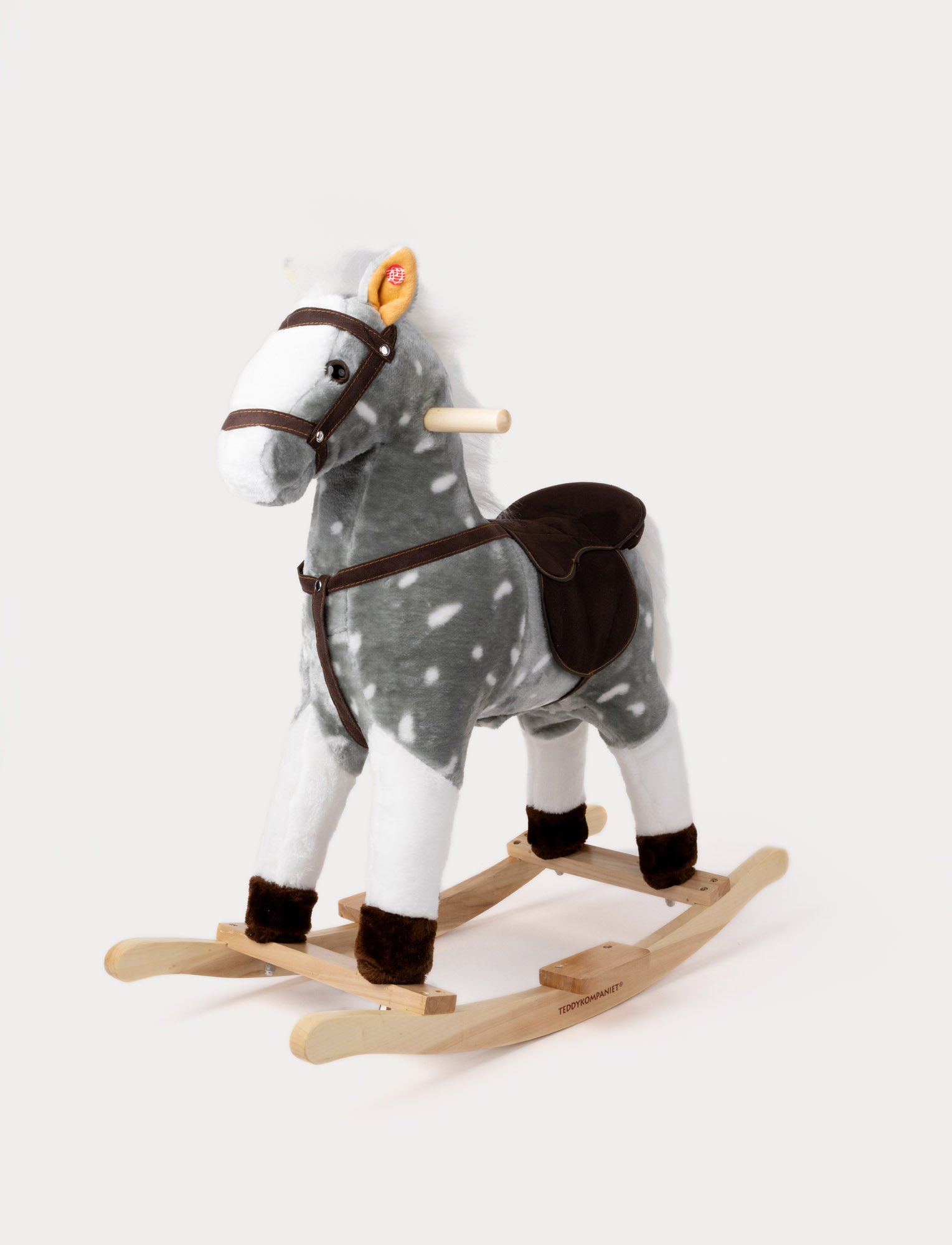  Image of Plush rocking horse with a grey and white spotted coat, brown saddle, and wooden base.