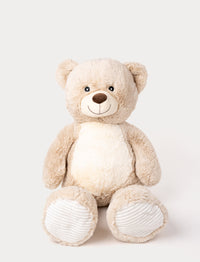 Soft beige teddy bear with a white belly, embroidered smile, and ribbed fabric on its paws.
