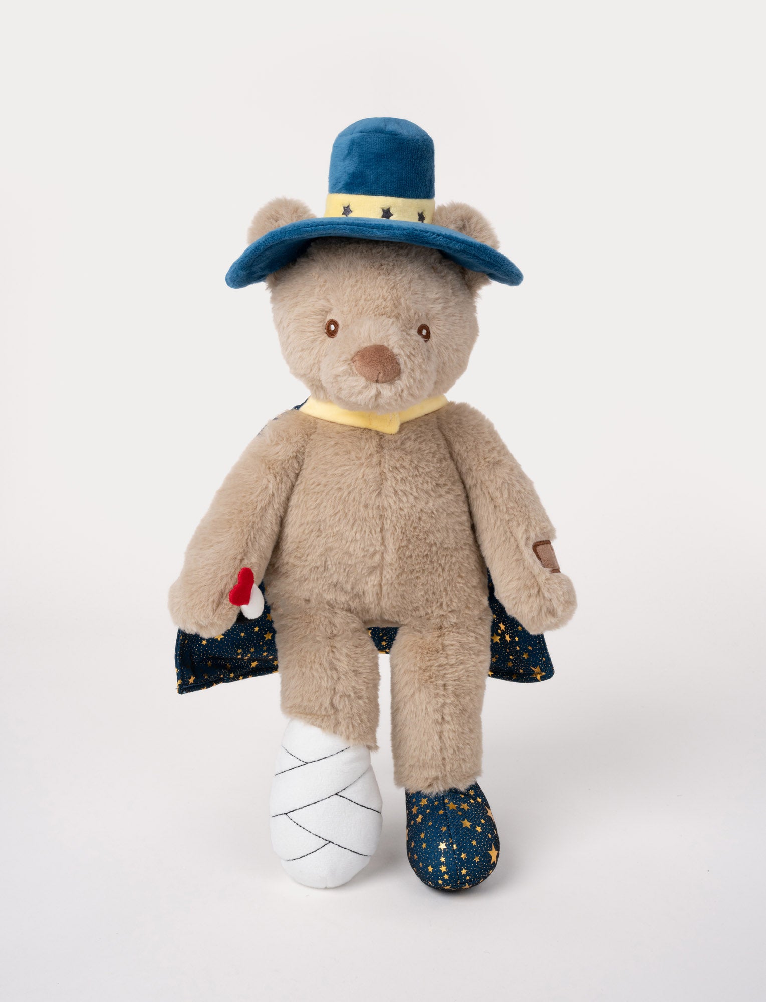  Image of Plush teddy bear dressed as a magician with a blue starry cape, hat, and wand, and one foot wrapped in a bandage.