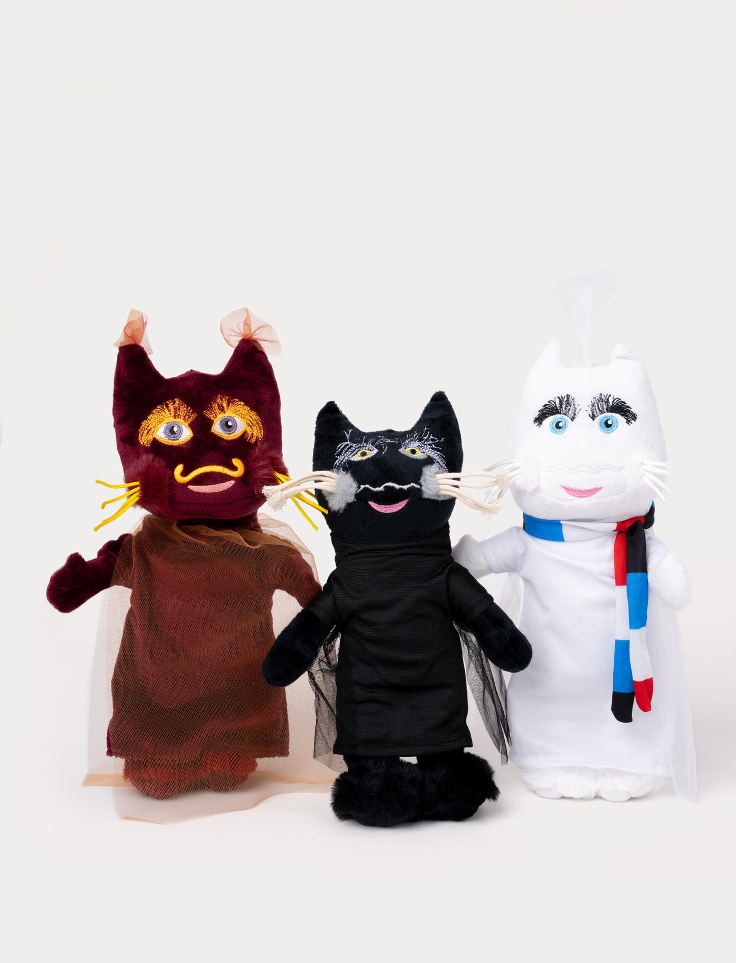 Three plush toys representing Sommarskuggan, Lavaskuggan, and Vinterskuggan, dressed in black, burgundy, and white outfits.
