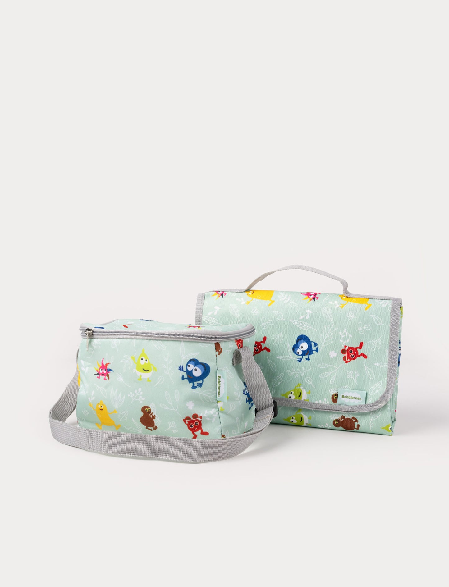 A lunch bag and a folded picnic blanket with Babblerna characters on a light green background.
