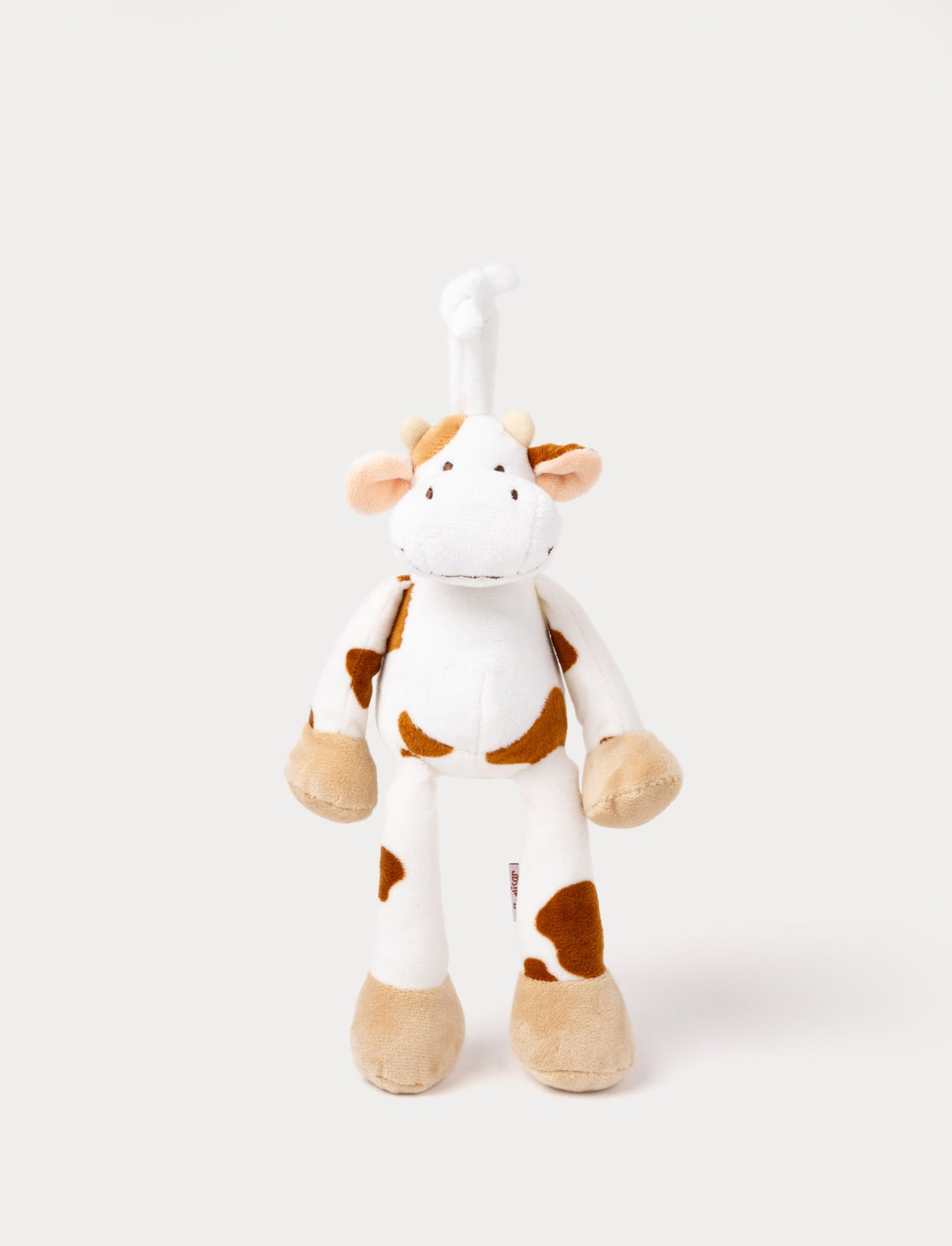A plush cow music box with brown spots, beige hooves, and a hanging loop.