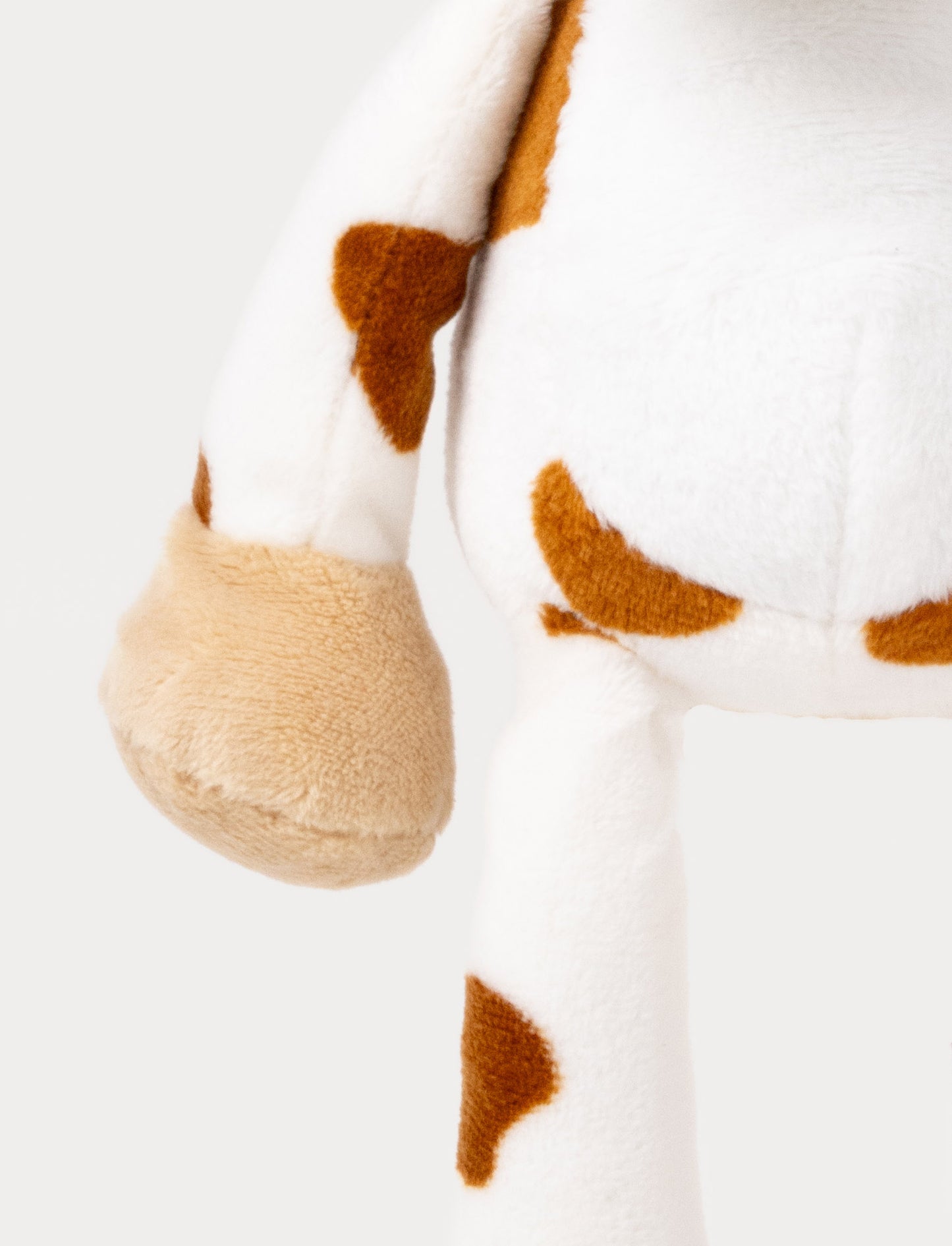 A plush cow music box with brown spots, beige hooves, and a hanging loop.