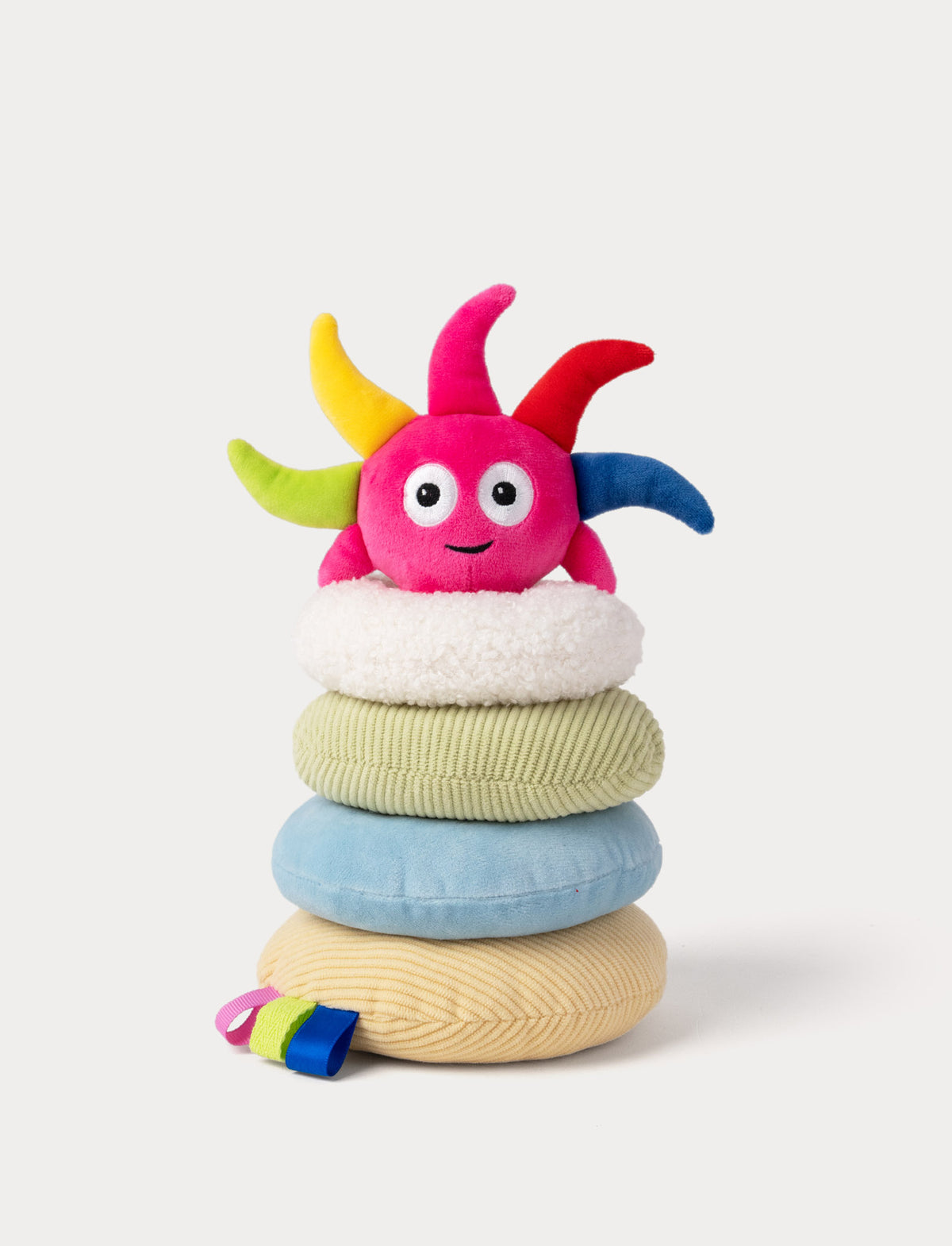 A colorful plush ring toy with Diddi from Babblarna. A fluffy white top cushion, stacked on top of three round textured cushions in pale green, light blue, and cream.