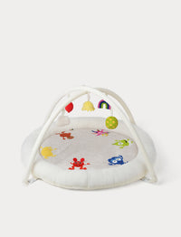 A baby sensory Babblarna play gym  The set includes a round white plush play mat decorated with colorful characters. White arch overhead with hanging sensory toys in red, yellow, rainbow, green, and pink, and a matching white padded base.