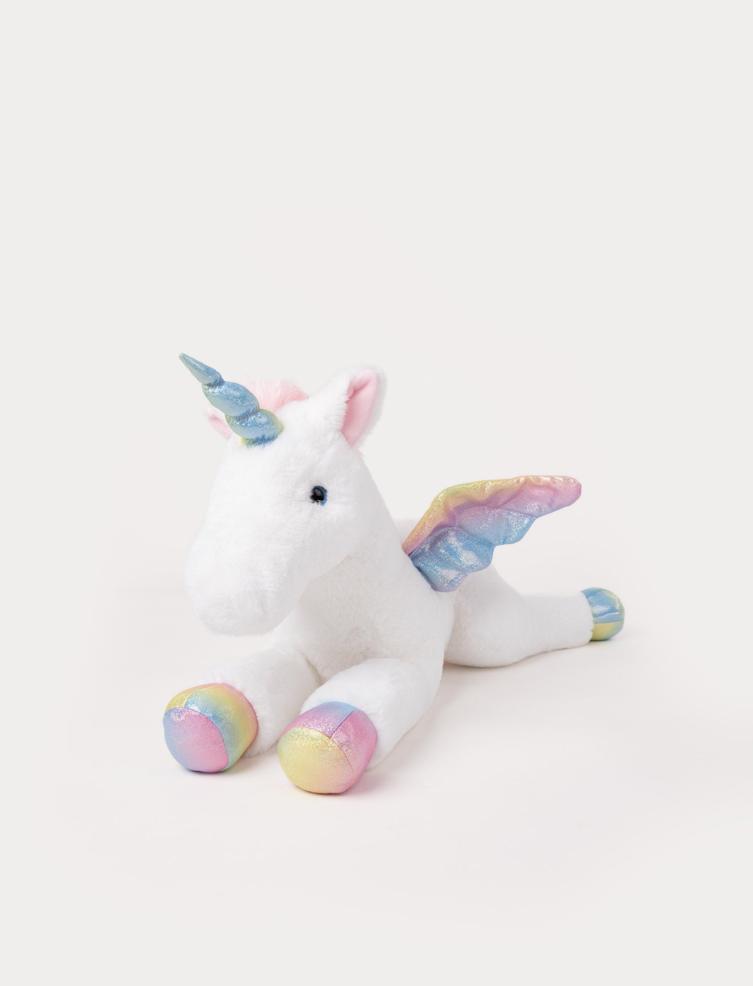  Image of White plush unicorn toy lying down with rainbow-colored hooves, shiny pastel wings, and a blue glittery horn