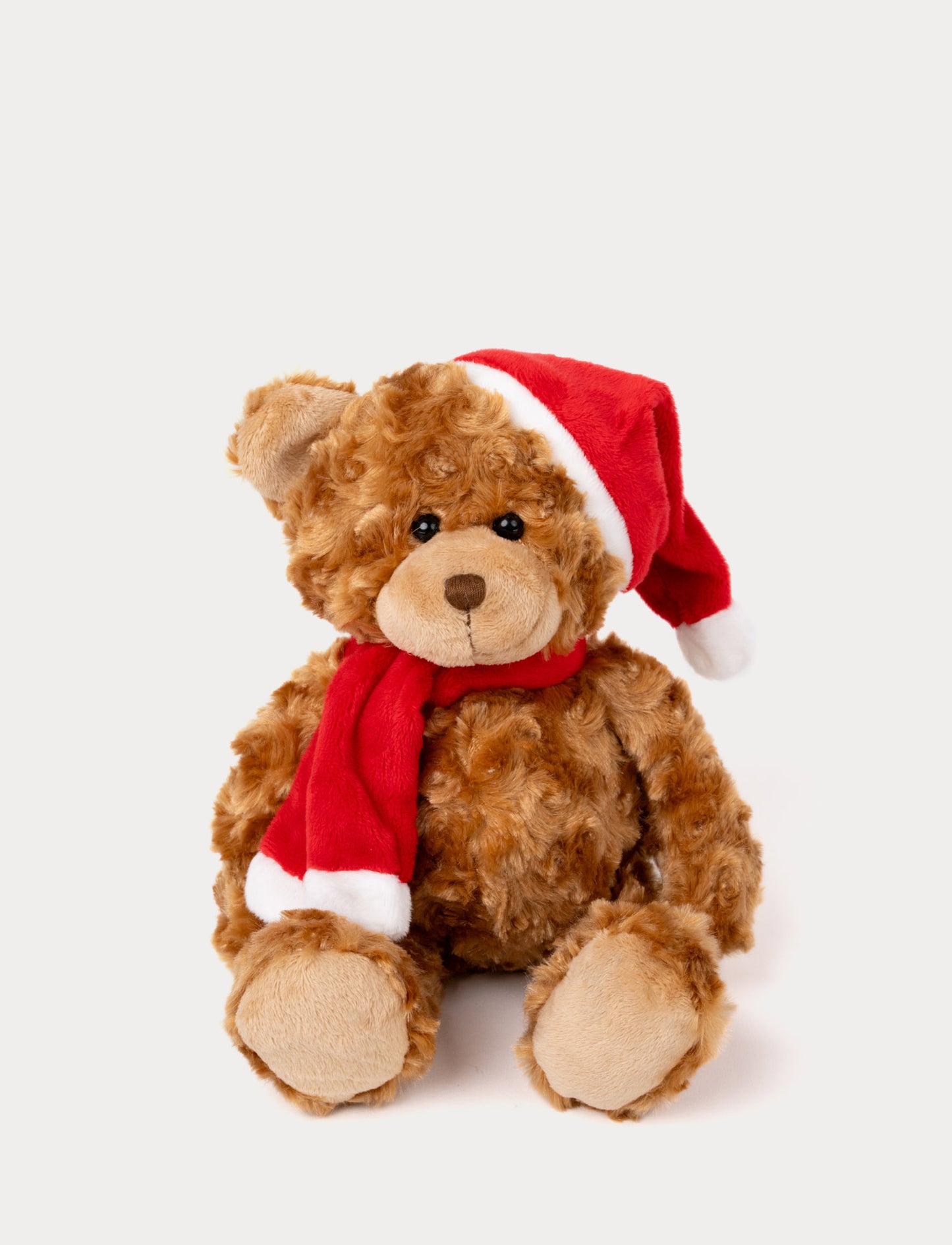 Curly brown teddy bear wearing a red Santa hat and matching red scarf with white trim.