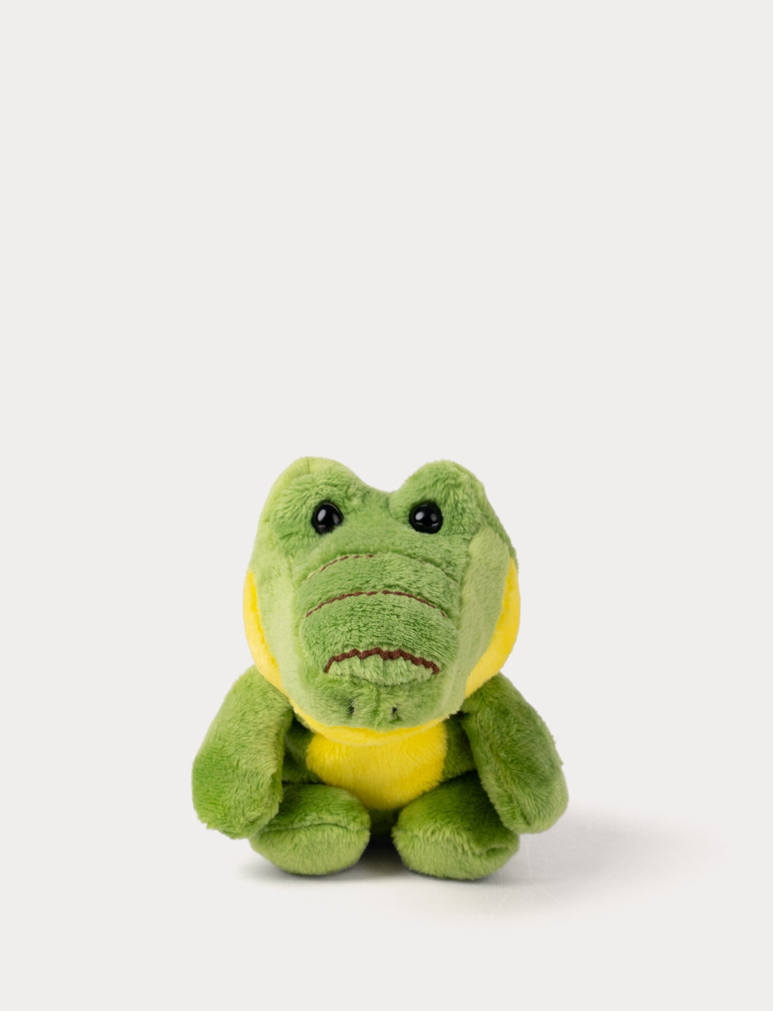  Image of Green plush crocodile toy with a yellow belly on a white background