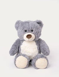 Soft grey teddy bear with a white belly, a stitched smile, and ribbed beige fabric on its paws.
