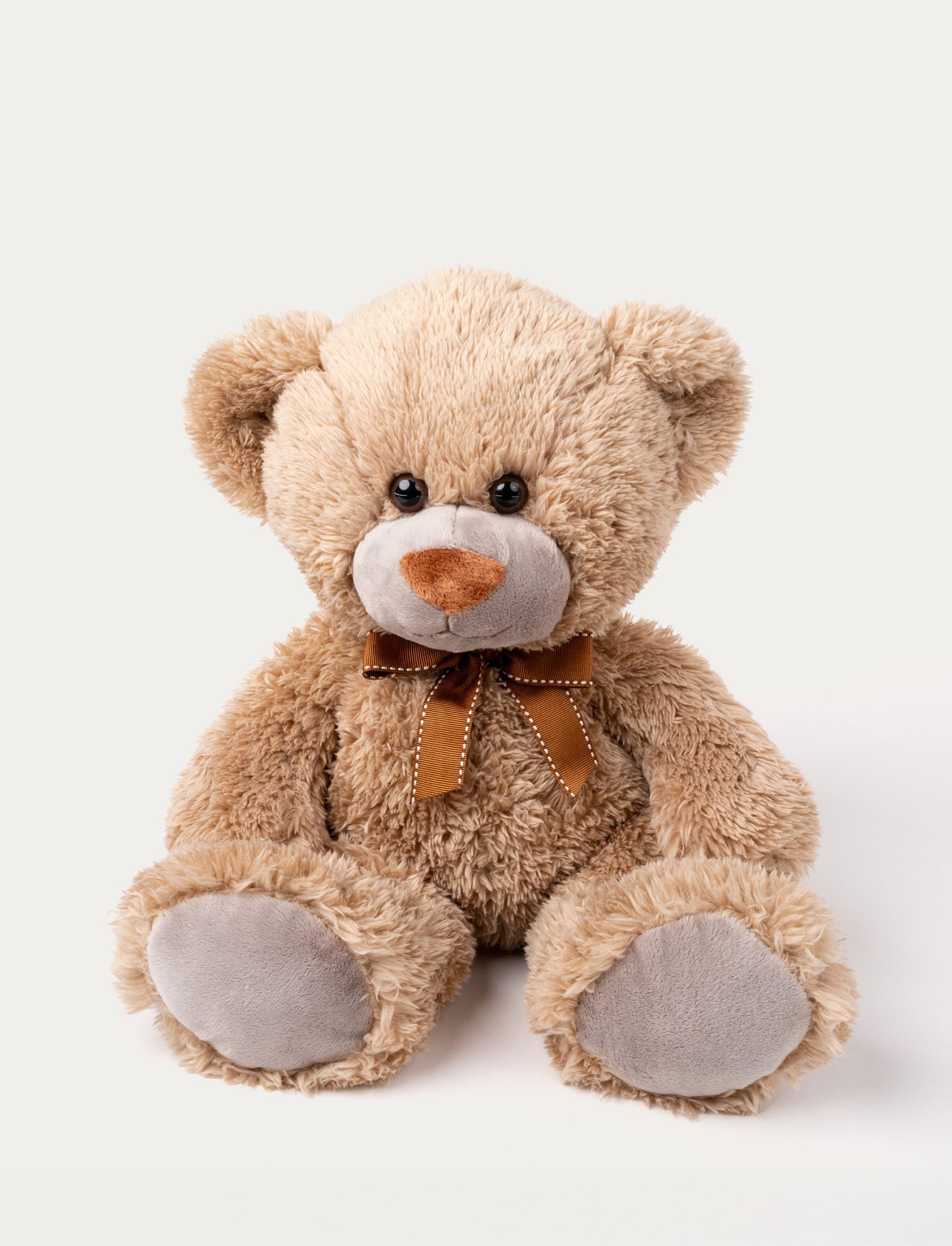  Image of Soft brown teddy bear with grey plush paws, a stitched brown nose, and a brown ribbon with white stitching around its neck.