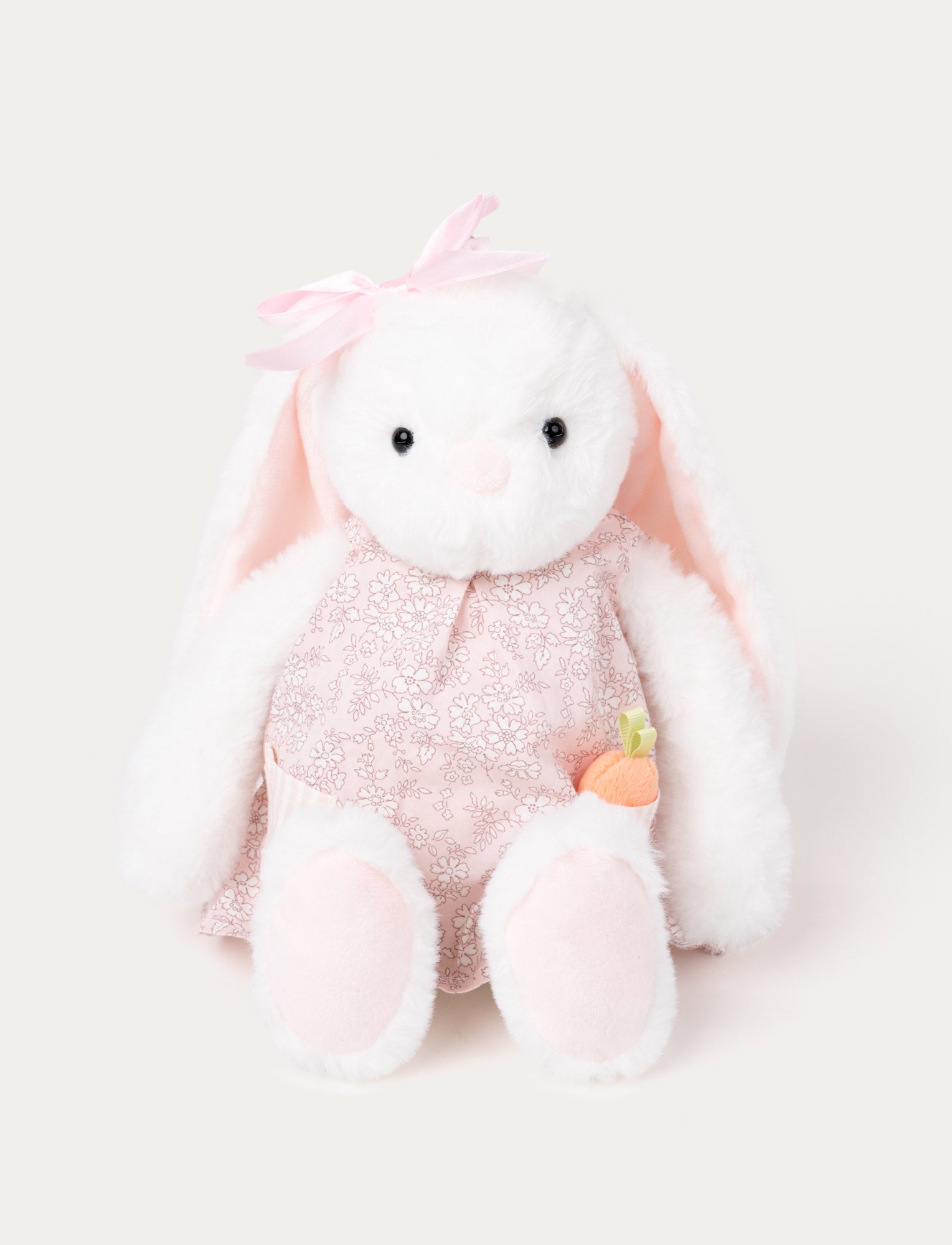  Image of Soft, white plush bunny with floppy ears, wearing a pink floral dress and a matching bow, holding a small plush carrot.