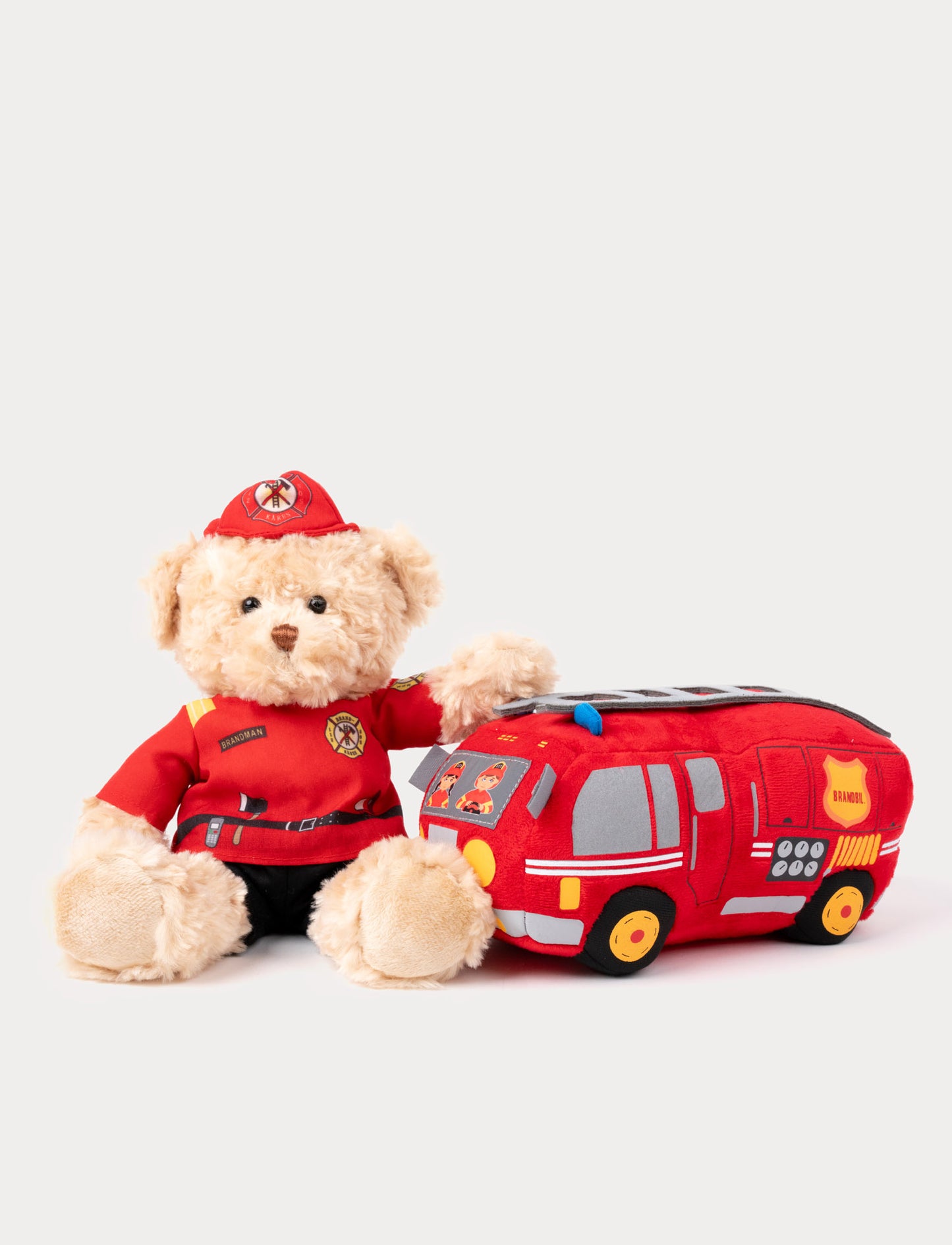 Plush firefighter teddy bear wearing a red uniform, sitting next to a soft red fire truck toy.