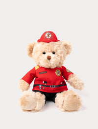 Soft, plush teddy bear with light beige fur, dressed as a firefighter in a red uniform with a matching hat and emblem details.
