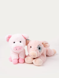 Two plush pig toys, one sitting with a pink snout and the other lying down with a gray patch around its eye.