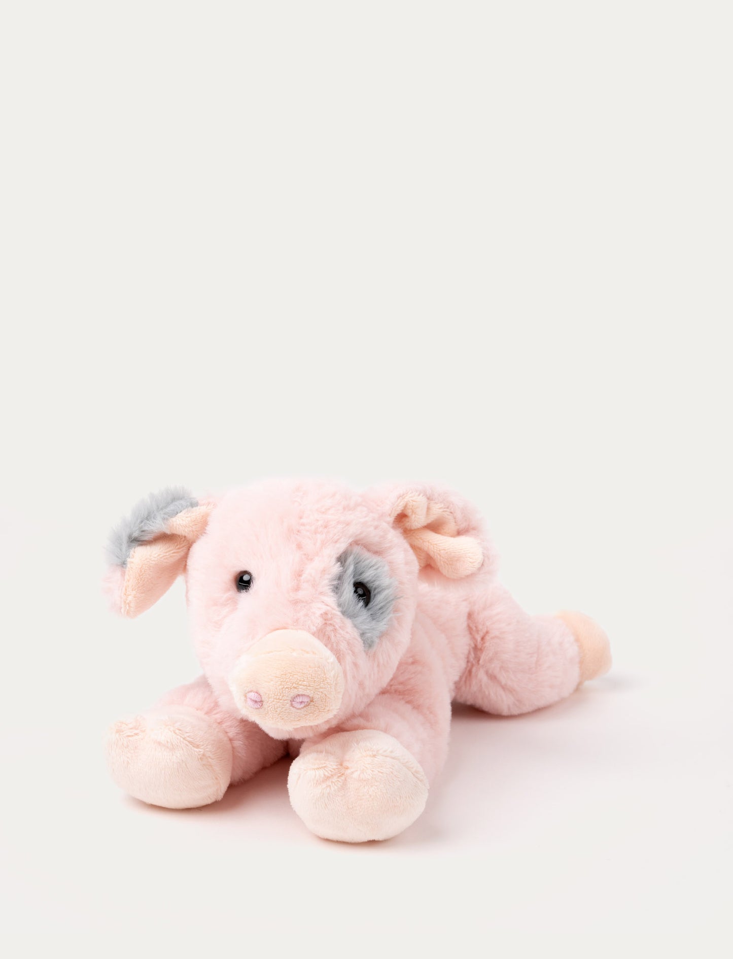 Soft plush pig with pink fur, a grey patch around one eye, floppy ears, and a curled tail, lying down.