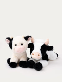 Two plush cow toys, one sitting with a pink nose and the other lying down with a black-and-white pattern.
