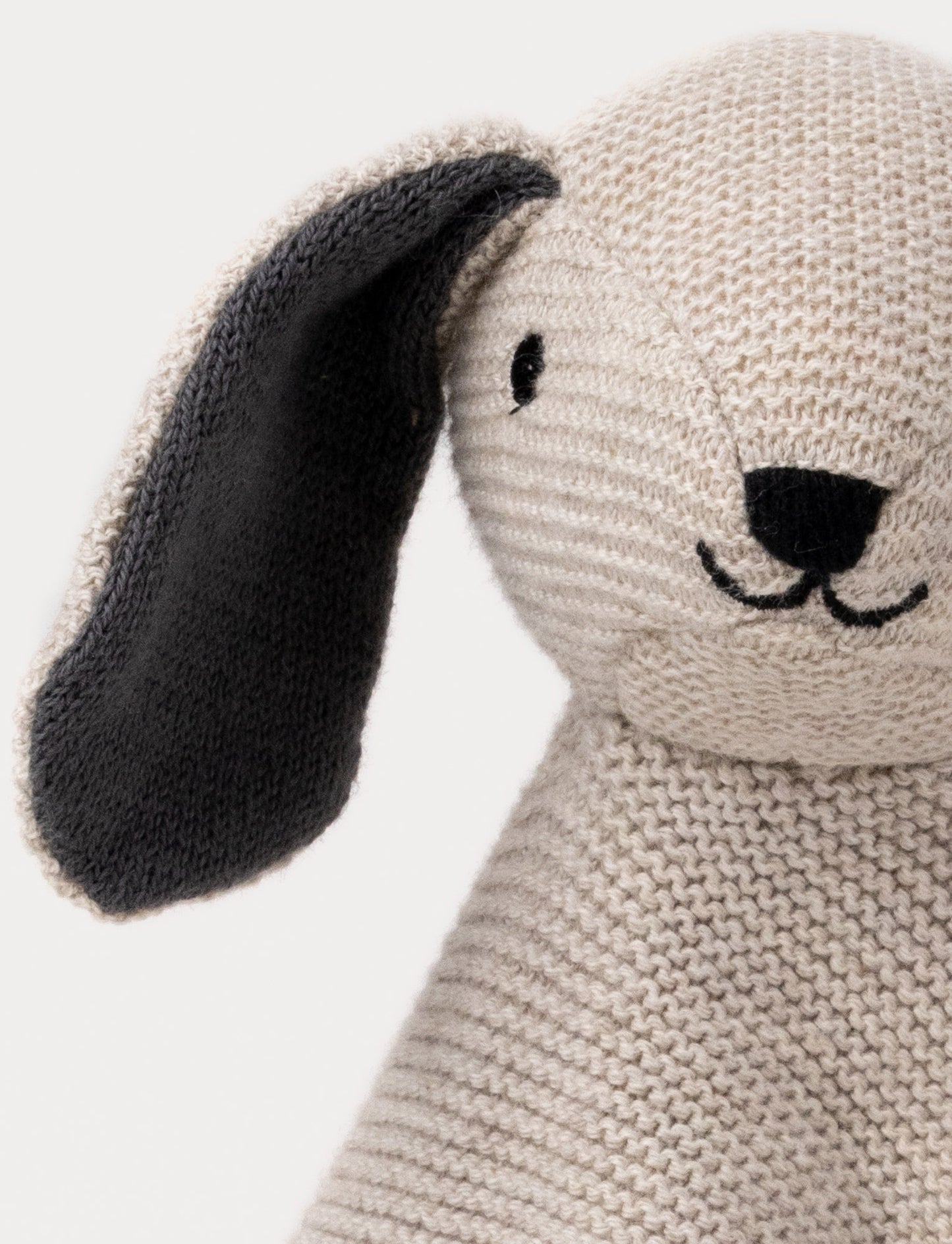 A knitted beige dog comforter with dark floppy ears, a stitched smiling face, and a soft textured fabric.