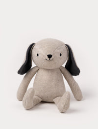 A knitted beige plush dog with dark floppy ears, a stitched smiling face, and a soft textured body.