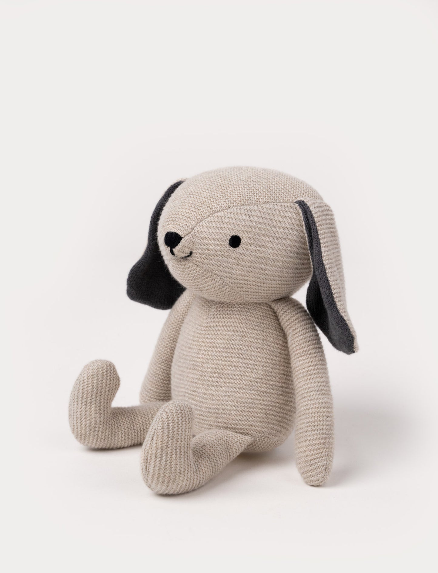 A knitted beige plush dog with dark floppy ears, a stitched smiling face, and a soft textured body.