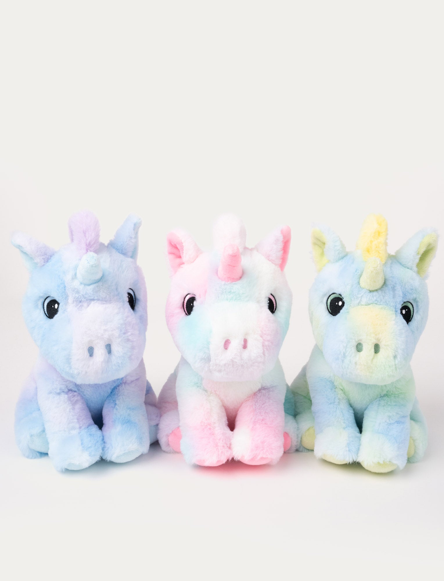  Image of Three plush unicorns in pastel colors, one purple, one pink, and one yellow, sitting side by side.