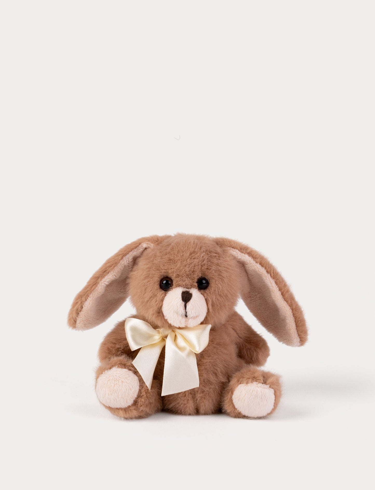 Brown plush bunny with a white bow on a light beige background
