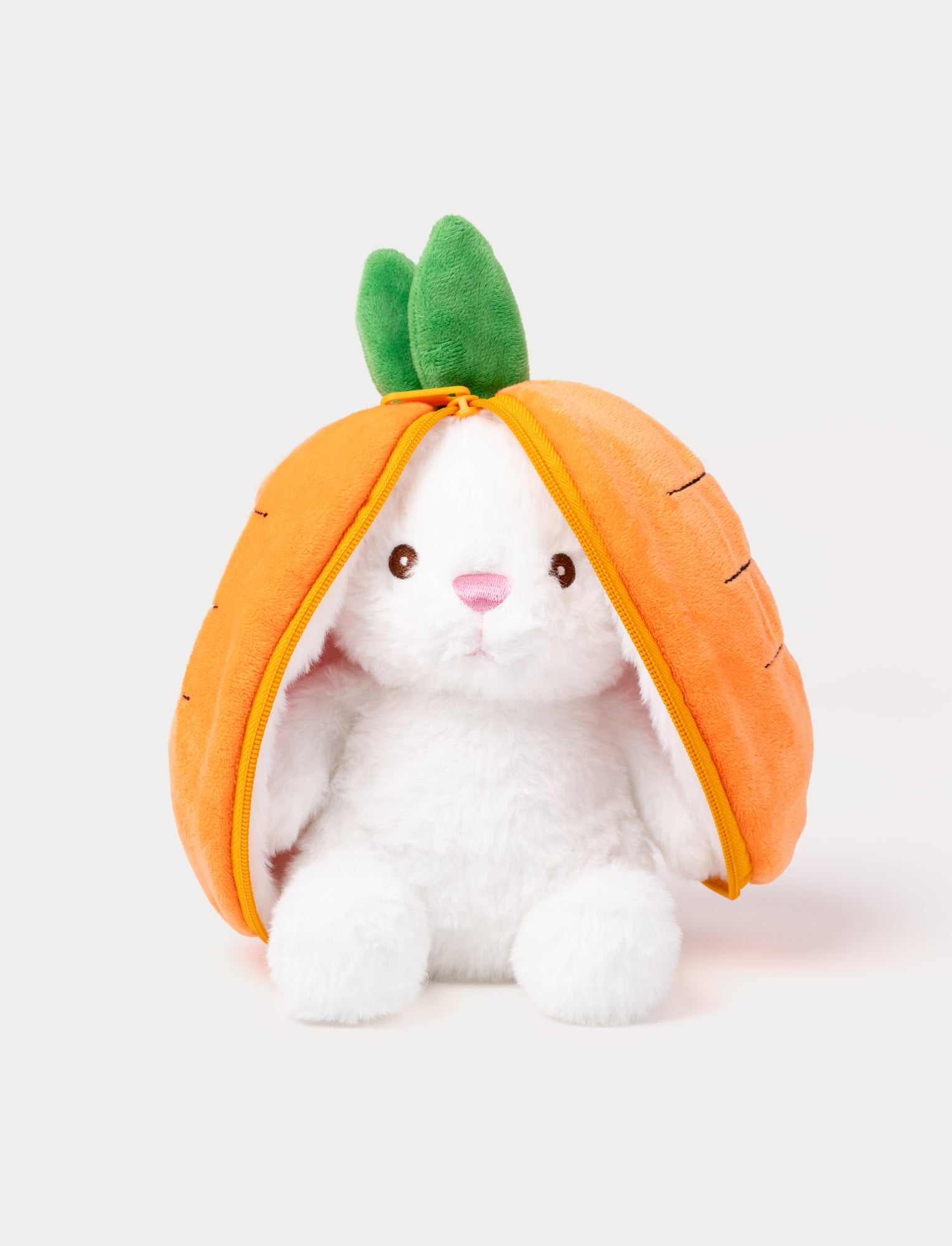  Image of White plush bunny sitting inside an orange carrot pouch with zipper and green leaves on top.