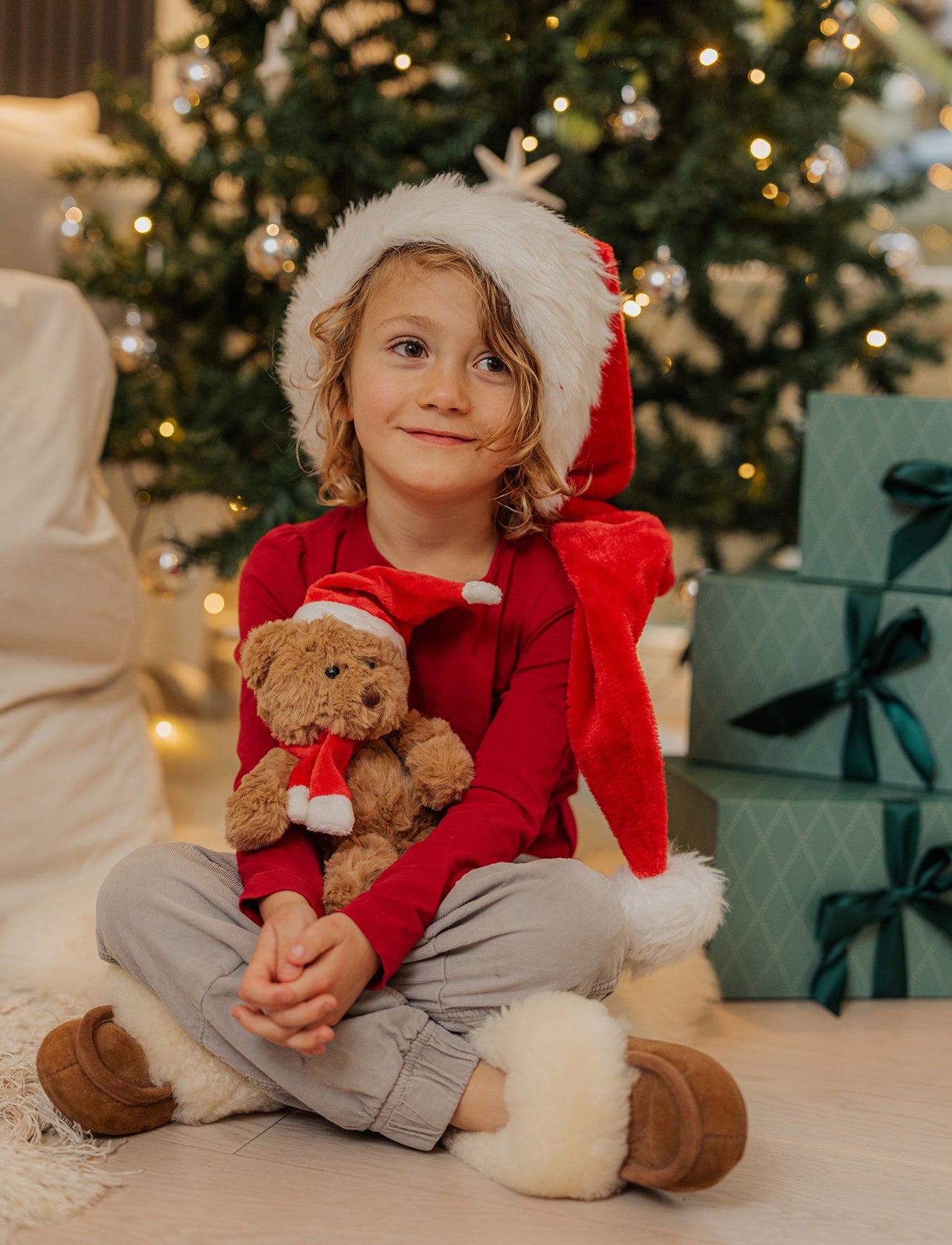 A teddy bear dressed in a santa outfit next to a christmas tree A teddy bear dressed in a santa outfit next to a christmas tree