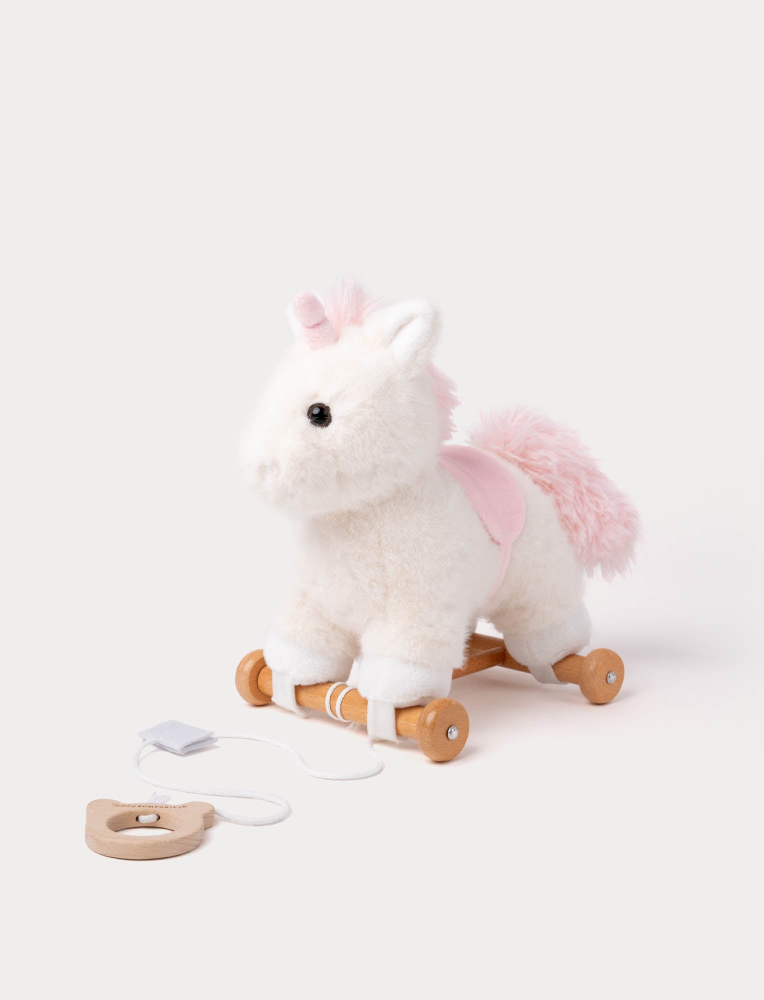  Image of Soft white plush pull-along unicorn toy with pink mane, saddle, wooden wheels, and string handle