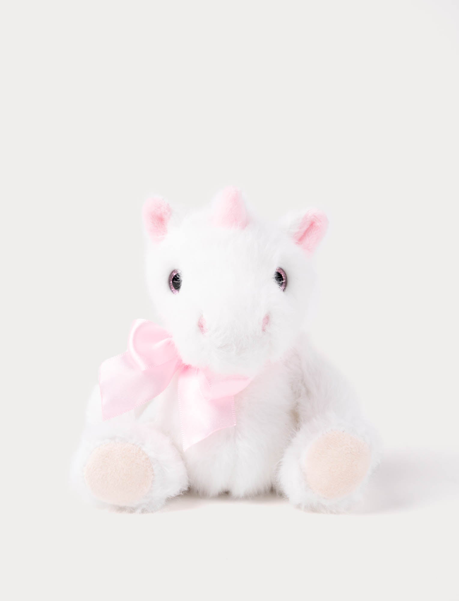  Image of White plush unicorn toy with pink bow and ears on a light gray background