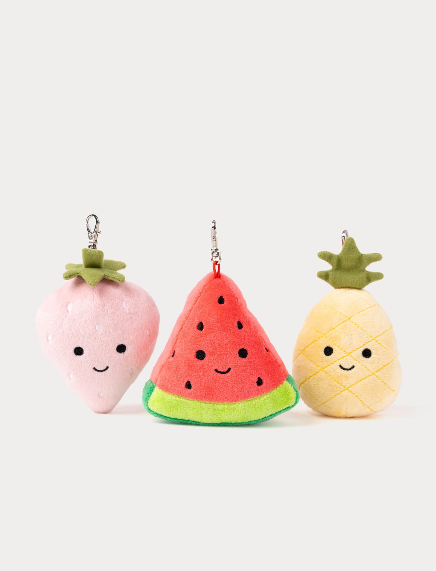 Three plush keychains shaped like a strawberry, watermelon, and pineapple on a white background