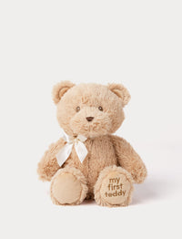 Beige teddy bear with a white bow and 'my first teddy' text on the paw